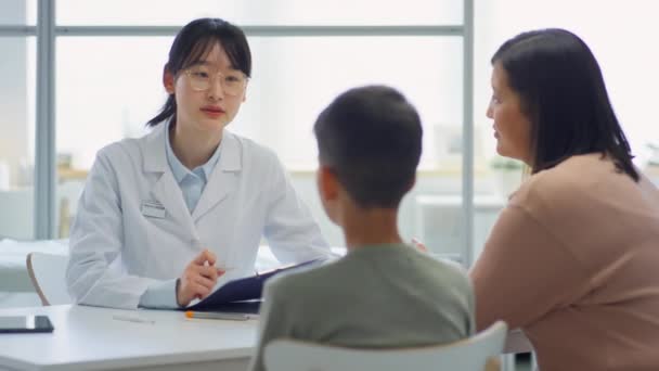 Beyaz Önlüklü Asyalı Kadın Çocuk Doktoru Klinikte Oturuyor Anne Ile — Stok video