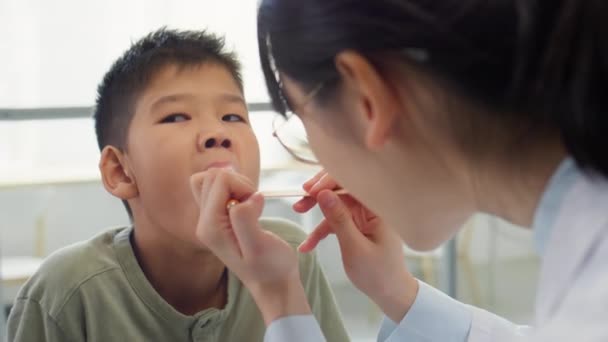 병원에 마비와 손전등 아시아 소년의 목구멍을 검사하는 여의사 — 비디오