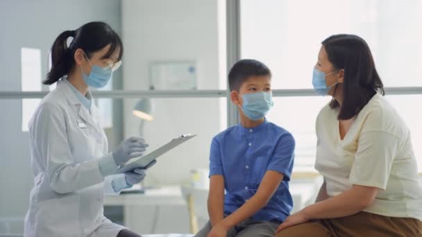 Ázsiai Anya Tinédzser Fiú Védő Maszk Orvosi Kanapén Klinikán Beszél — Stock videók
