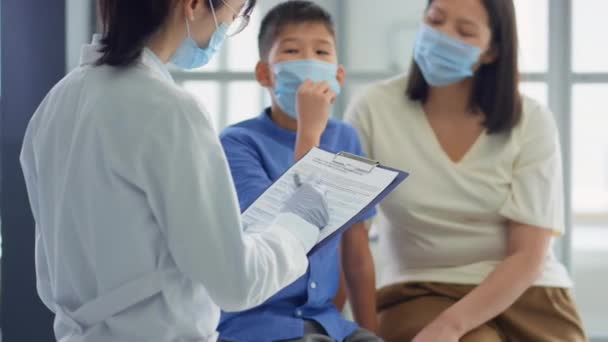 마스크를 소아과 의사가 코로나 바이러스가 유행하는 아시아 어머니와 상담하는 클립보드에 — 비디오