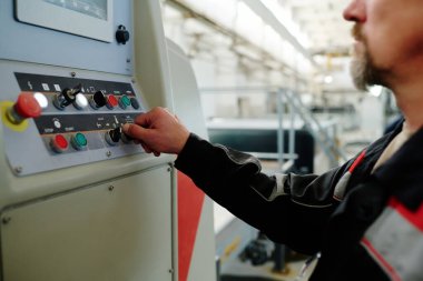 Makinedeki düğmelere basan ve fabrikadaki işi kontrol eden üniformalı mühendislere yakın çekim