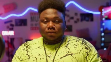 Genç Afrikalı Amerikalı müzisyenin portresi, renkli neon ışıkla aydınlatılmış kayıt stüdyosunda kameraya poz veriyor.