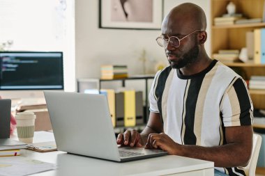 Ciddi bir Afrikalı Amerikalı programcı bilgisayarında kodlar yazıyor. IT ofisinde oturuyor.
