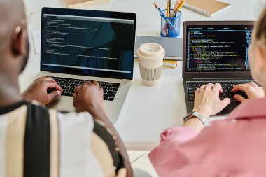 Ofiste otururken bilgisayar programları için dizüstü bilgisayarlara güvenlik kodları yazan meslektaşların arka görünümü