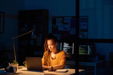 Genç müteahhit iş yerinde otururken dizüstü bilgisayarda yazı yazıyor, gece yarısına kadar ofisinde çalışıyor.