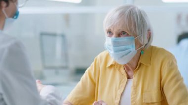 Tek kullanımlık yüz maskesi takan yaşlı bir kadın, kadın doktorla kovid salgın sırasında kliniğe giderken tartışıyor.