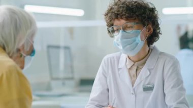 Korunaklı maskeli kadın doktorun Coronavirus salgını sırasında klinikte çalışırken kıdemli bir hastayla konuşması.