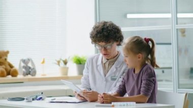 Kadın doktor ve küçük kız dijital tablet kullanıyor ve muayenehane sırasında tartışıyorlar.
