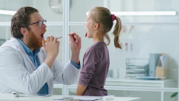 男儿科医生在诊所为小女孩进行体格检查时 使用舌头抑制剂和手电筒 — 图库视频影像