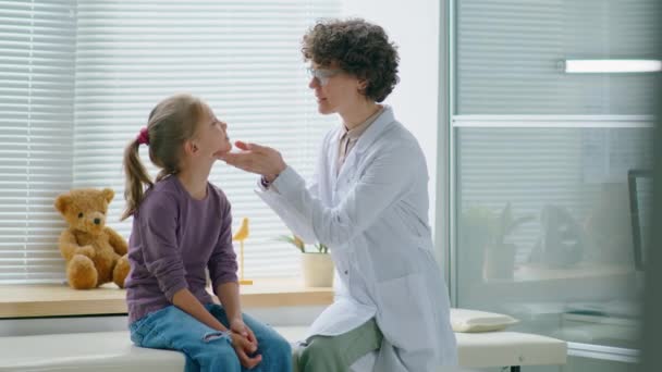 女の子の首にリンパ節に触れる女性小児科医と彼女に話します間に健康診断でクリニック — ストック動画
