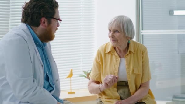 白发老年妇女坐在诊所的医疗沙发上 与男医生交谈 — 图库视频影像