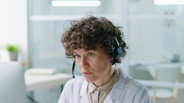 オンラインビデオ通話で何かを説明するヘッドセットの女性開業医は クリニックで患者とオンラインで作業しながら コンピュータ上で — ストック動画