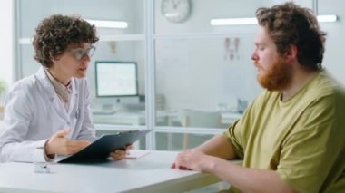 Kadın doktora tıbbi geçmişini veren ve klinikte kilo kaybı hakkında konsültasyon alan genç şişman bir adam.