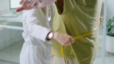 Kadın doktorun, erkek hastanın belini şişmanlıkla ölçerken, klinikte ona sağlık kontrolü yaparken yukarı doğru eğilmesini.