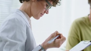 Kadın doktoru, erkek hastayı dinlerken ve klinikteki tıbbi danışmanlık sırasında not alırken yukarı kaldır.