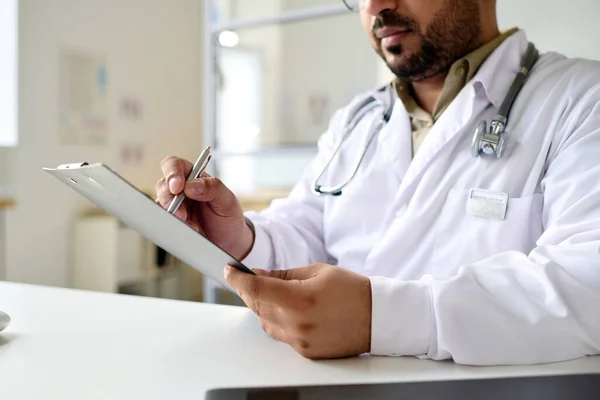 白衣を着た医者が職場に座りながら患者の処方箋を書いている — ストック写真
