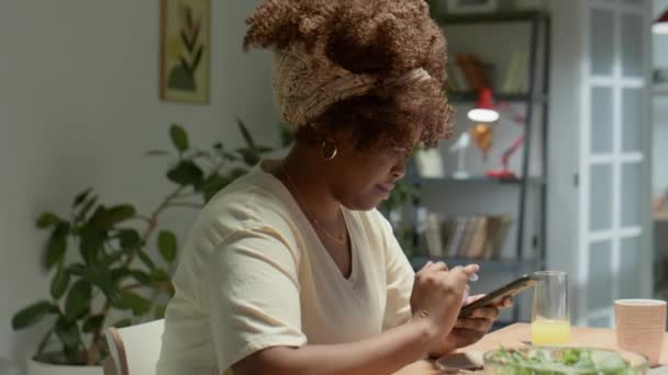Zdjęcie Łukowe Młodej Afroamerykanki Piszącej Smartfonie Siedzącej Przy Stole Domu — Wideo stockowe