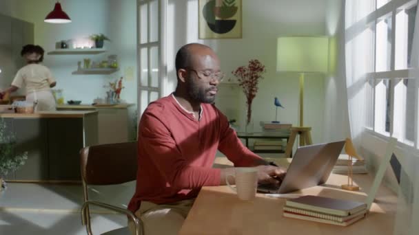 아프리카 미국인 남자가 저녁에 집에서 노트북으로 일하고 마시며 주방에서 식사를 — 비디오