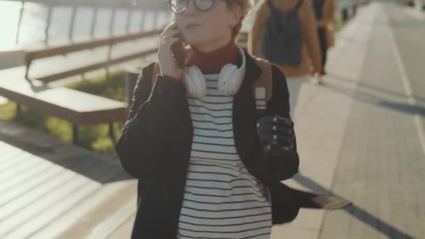 阳光明媚的城市里 一个有假肢的女孩在河堤上散步 用手机交谈 拍摄她的倒立镜头 — 图库视频影像