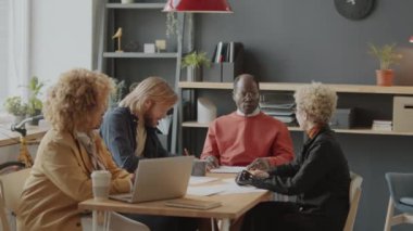 Modern ofisteki toplantı masasında oturan, not alan, dizüstü bilgisayar kullanan ve üst düzey Afrikalı Amerikalı yöneticilerle proje tartışan çeşitli iş adamları.