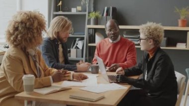 Protez kollu genç beyaz iş kadını çok ırklı meslektaşlarını dinliyor ve ofis toplantısında dizüstü bilgisayarda yazı yazıyor.