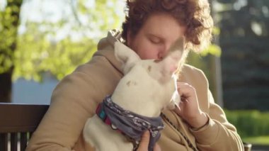 Neşeli adam parkta bankta oturuyor, gülümsüyor, güzel staffordshire teriyeri köpeğini okşuyor ve ona atıştırmalık veriyor.