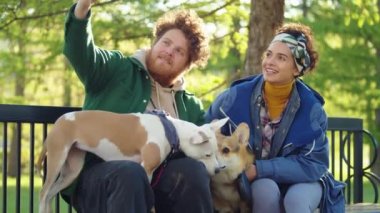 Kadın ve erkek parkta bankta oturuyor, akıllı telefon kamerasına gülümsüyor ve sevimli köpeklerle selfie çekiyorlar.
