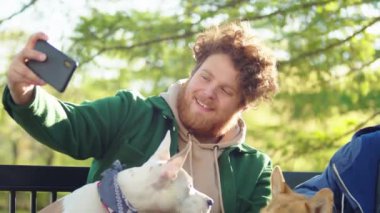 Sevgili Corgi ve Personel Teriyeri 'yle parkta oturan ve akıllı telefonlu selfie çeken erkek ve kadın arkadaşlar.