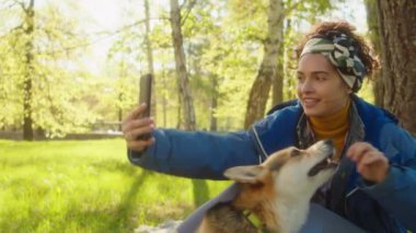 Genç ve güzel bir kadın parkta akıllı telefonuyla selfie çekerken tatlı Corgi Dog 'a ikramda bulunuyor.