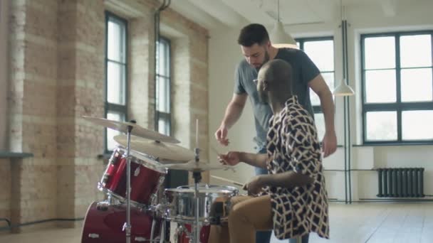 白人音楽教師がアフリカ系アメリカ人男性にスタジオでドラムレッスン中にドラムスティックを保持する方法を説明 — ストック動画