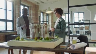 Afrika kökenli Amerikalı erkek mimarın beyaz kadın meslektaşla ofis projesinde çalışırken modellerin tasarımını tartışırken görüntüsünü yakınlaştırın.