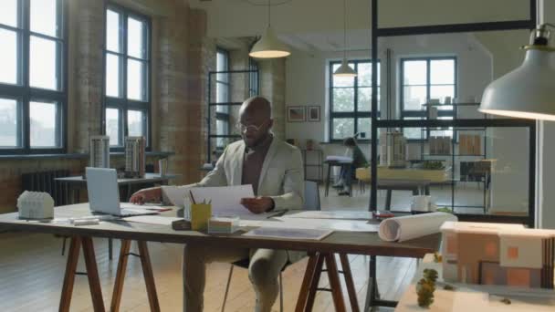 放大了非洲裔美国建筑师坐在现代开放办公室的办公桌前检查纸质图纸的镜头 — 图库视频影像