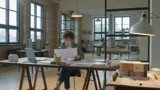 放大女性建筑师的照片 卷曲短发 检查图纸 在现代舒适的办公室里工作时使用笔记本电脑 — 图库视频影像