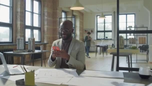 在建筑办公室的工作环境中 一个快乐的黑人商人一边用手机发短信一边微笑 放大了镜头 — 图库视频影像