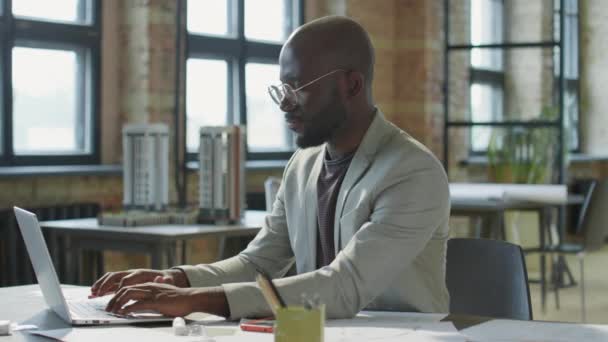 建筑办公室里穿着时髦休闲装和眼镜在笔记本电脑上工作的黑人商人的弧形照片 — 图库视频影像