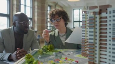 Beyaz kadın mimar Afrikalı Amerikalı erkek müşteriye emlak geliştirme modeli sunuyor.
