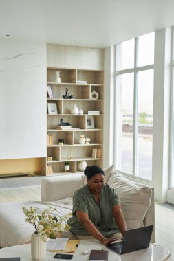 Evde dizüstü bilgisayarda çalışan Afrikalı Amerikalı bir kadının dikey görüntüsü