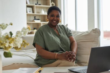 Evde dizüstü bilgisayarla çalışırken kameraya gülümseyen Afrikalı Amerikalı kadın portresi