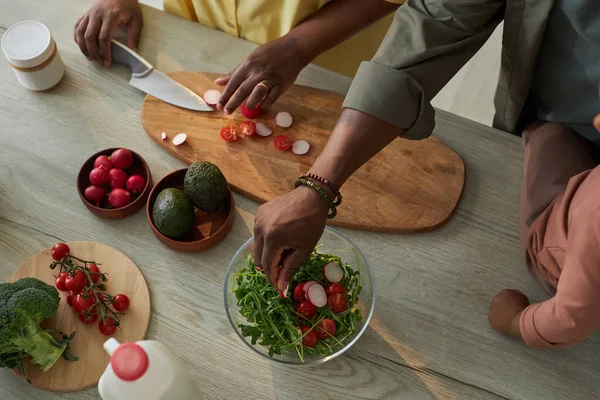 stock image Top view of woman cutting vegetables on board for salad with her husband helping her