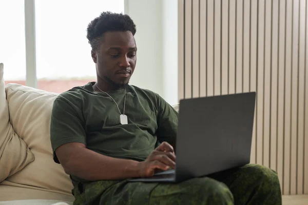 アフリカ系アメリカ人兵士が自宅のソファに座りながらノートパソコンを使う — ストック写真
