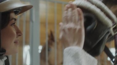 Kapalı el kamerasıyla genç mutlu bir kadının kaskla gülüşünü ve onu ahırda okşarken at burnuna dokunuşunu çek.