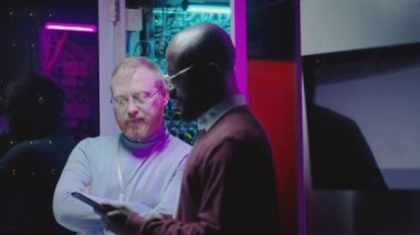 Beyaz ve Afro-Amerikan ağ destek mühendisleri veri merkezinin sunucu odasında dijital tablet hakkında bir şeyler tartışıyorlar.