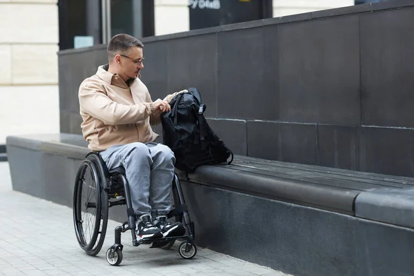 Молодий Чоловік Відкриває Рюкзак Сидячи Інвалідному Візку Місті — стокове фото