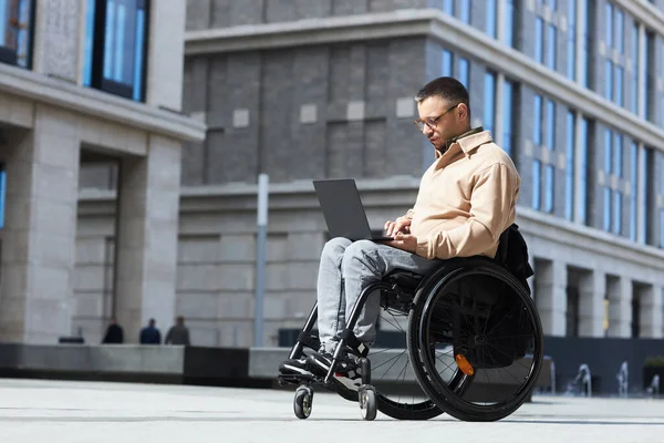 Młody Mężczyzna Niepełnosprawnością Siedzi Wózku Inwalidzkim Pisze Laptopie Mieście — Zdjęcie stockowe