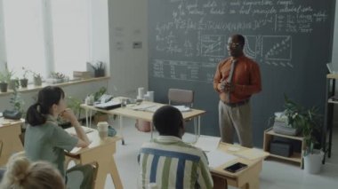 Afrika kökenli Amerikalı profesörün çok ırklı öğrencilere üniversitede ders verirken tahtadaki formülleri açıklarken çekilen görüntüleri.