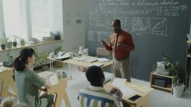 Afrika kökenli Amerikalı bir profesörün, üniversite sınıfında ders verirken etnik çeşitliliğe sahip bir grup öğrenciyle konuşurken çekilmiş görüntüleri.