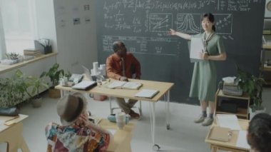 Asyalı kız öğrencinin sınav kağıtlarını tutarken ve çeşitli grup arkadaşlarına ve üniversite dersi sırasında Afrikalı Amerikan profesörüne konuşma yaparken aşağı eğilin.