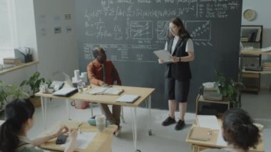 Kadın öğrencinin sınav kağıtlarını tutarken ve grup arkadaşlarının ve Afrika kökenli Amerikalı profesörün önünde sunum yaparken çekilen pozu.