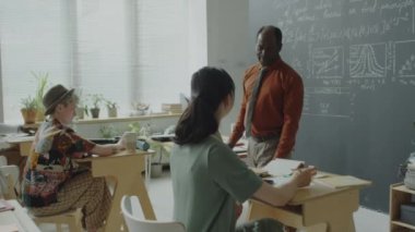 Sınıfta sıraların arasında yürüyen Afrikalı Amerikalı bir profesör ve üniversitede sınava giren öğrencilere bakıyor.