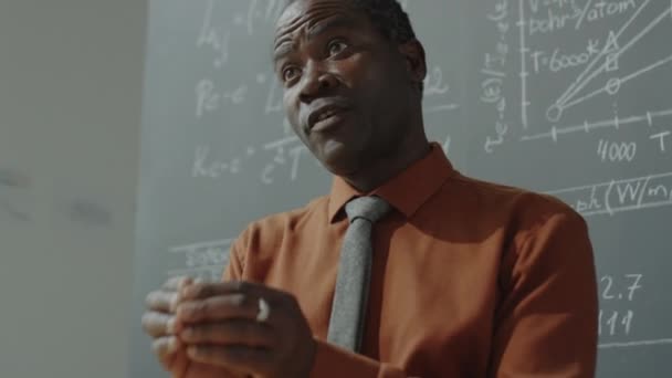 低角度拍摄的非裔美国教授站在黑板旁边 上面有数学公式 并解释了大学的课程 — 图库视频影像